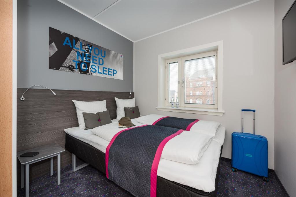 A compact hotel room with a made bed, a window and a suitcase in the corner.