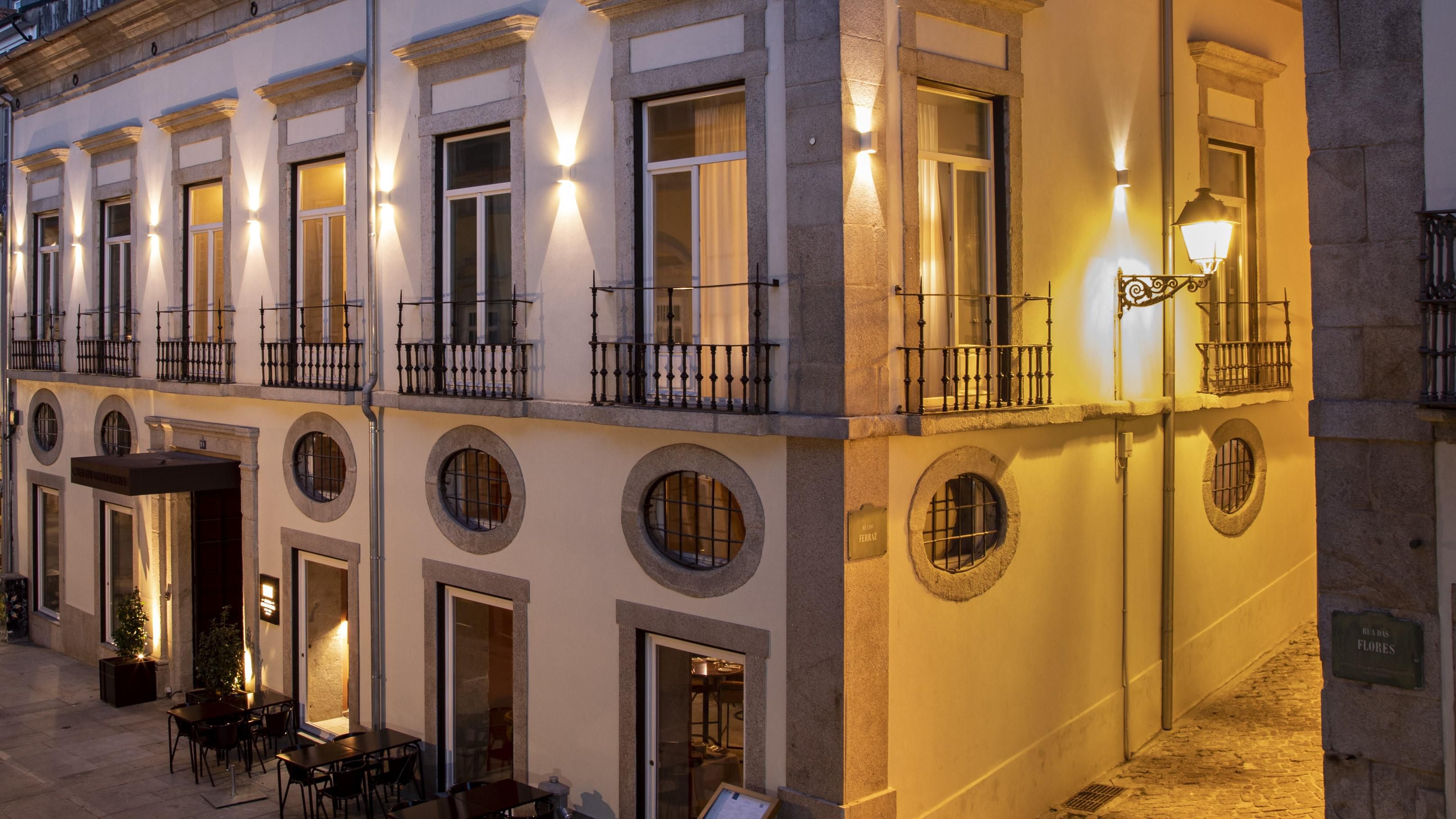 A corner city house at night, with tall windows, a cobbled alley and tables on the pavement.
