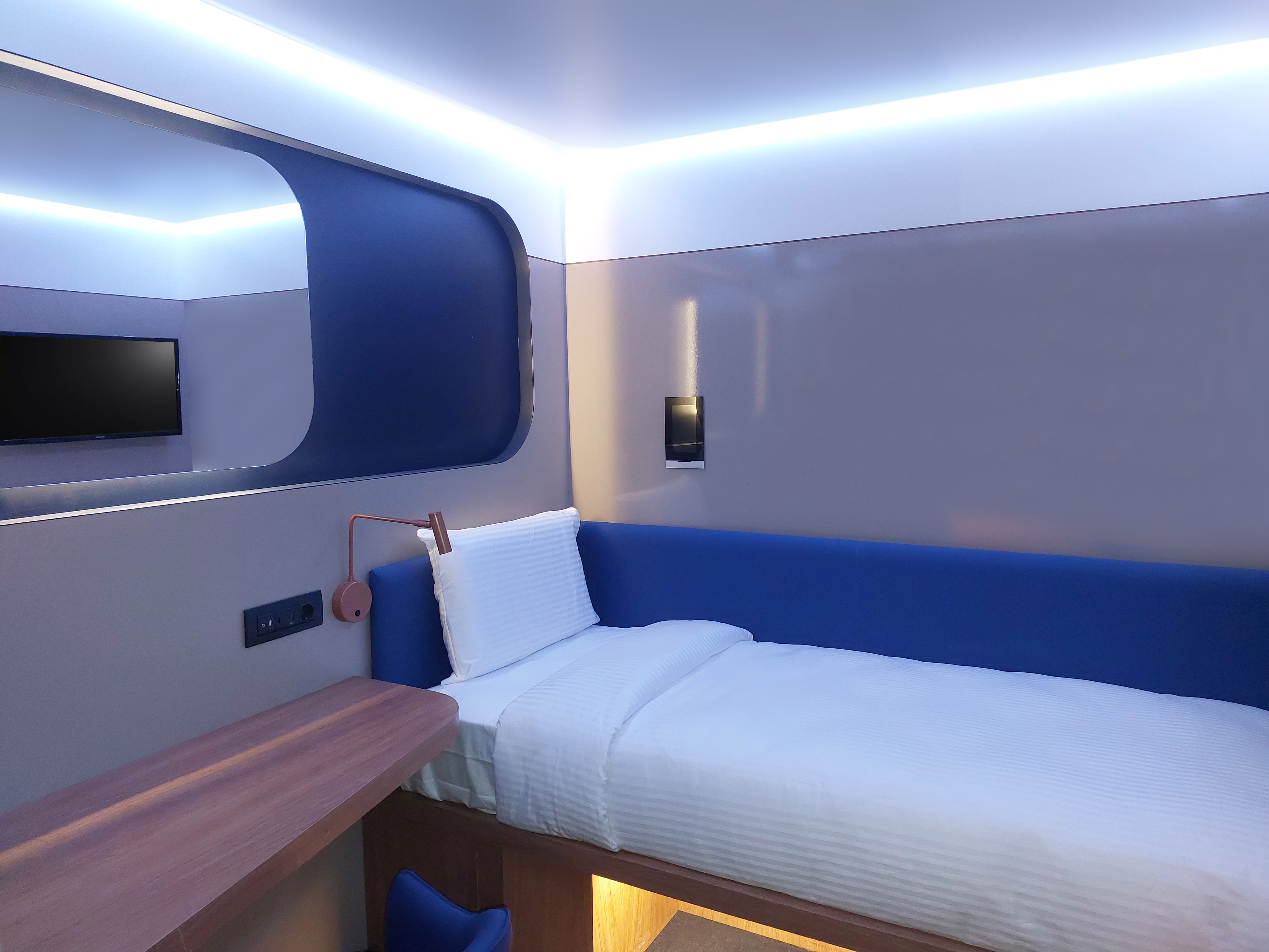 A compact cabin room with a built-in bed, a wall desk and a mirror.